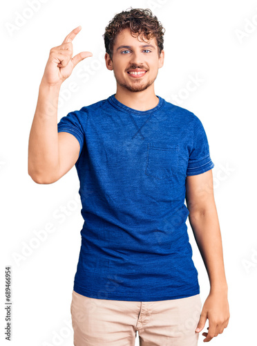 Young handsome man with curly hair wearing casual clothes smiling and confident gesturing with hand doing small size sign with fingers looking and the camera. measure concept.