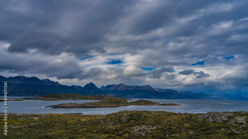 The harsh landscape of southern Patagonia. The islands in the Beagle Channel have low-growing sparse vegetation. In the distance, against the sky and clouds the picturesque mountain range,  Andes