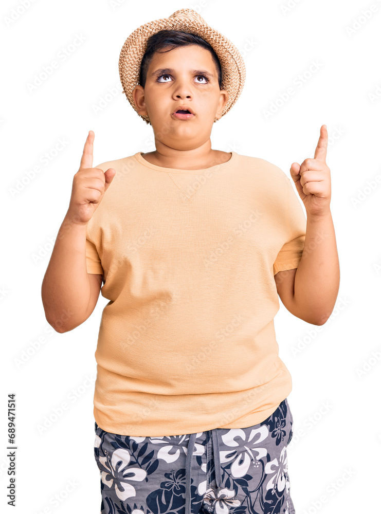 Little boy kid wearing summer hat and hawaiian swimsuit amazed and surprised looking up and pointing with fingers and raised arms. Little boy kid wearing summer hat and hawaiian swimsuit amazed and surprised looking up and pointing with fingers and raised arms.