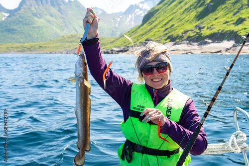 A joyful and proud female angler shows off her impressive catch in the beautiful Norwegian Sea, demonstrating her love for the leisure pursuit of fishing with great enthusiasm.
