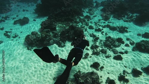 Freediver in wetsuit hover over shallow depth around coral white sand seabed, slow motion photo