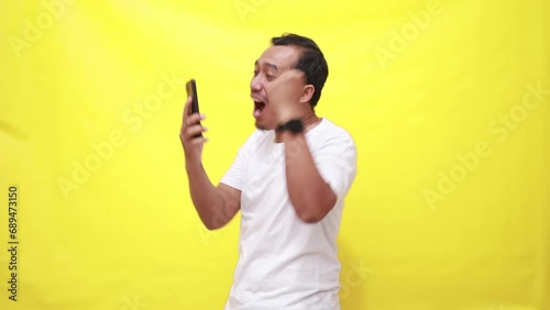 Smartphone, excited with asian man isolated yellow background in studio, celebration and social media giveaway. Happiness, cheers and winning with online competition, dancing for reward photo
