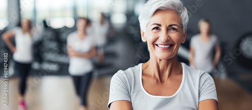 Cheerful senior woman with exercising people in the background at fitness studio.