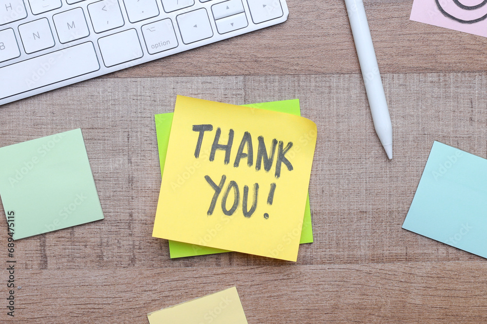Thank You text on sticky notes with office stationery over wooden