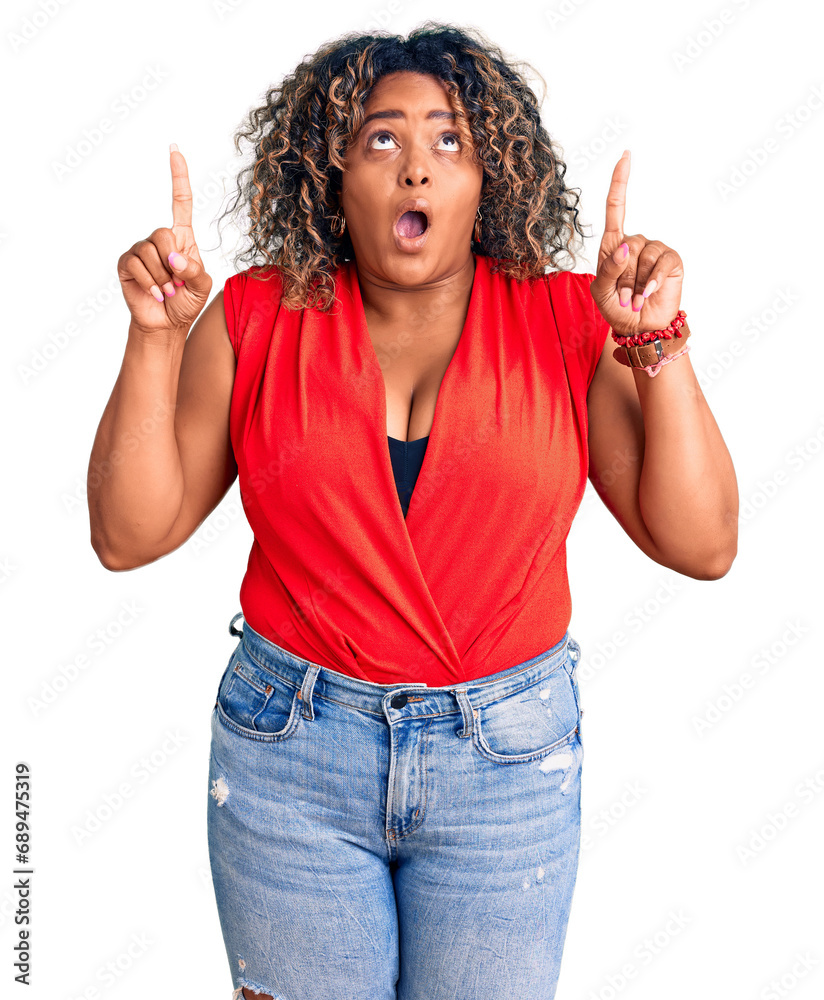 Young african american plus size woman wearing casual style with sleeveless shirt amazed and surprised looking up and pointing with fingers and raised arms. Young african american plus size woman wearing casual style with sleeveless shirt amazed and surprised looking up and pointing with fingers and raised arms.