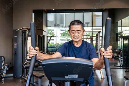 Asian old man in the 70s or 80s to step on flywheel training helping leg muscle strength, Healthy older man training or a quick warm up in the fitness room. lifestyle or health of senior man