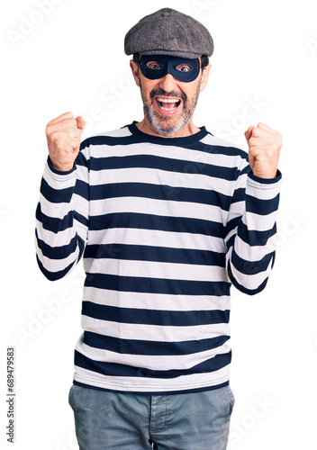 Middle age handsome man wearing burglar mask celebrating surprised and amazed for success with arms raised and open eyes. winner concept. © Krakenimages.com