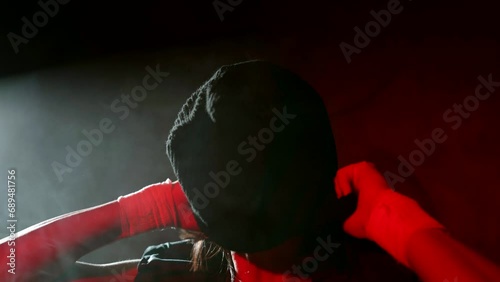 woman gangster or soldier putting black balaclava on her head in dark room or basement, closeup