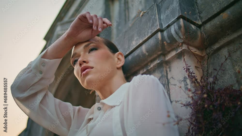 Attractive model looking camera raising hand over head at medieval wall close up