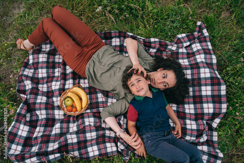 Hispanic woman laying on plaid with son enjoying picnic being in sad mood missing husband. Frustration