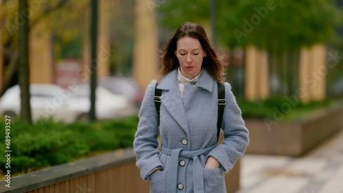 portrait of middle-aged townswoman with smartphone in hands walking in city street in autumn photo