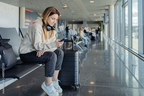 Woman use smartphone and earphones while waiting for her flight, student girl listening to music or podcast at the airport while waiting for a flight. photo