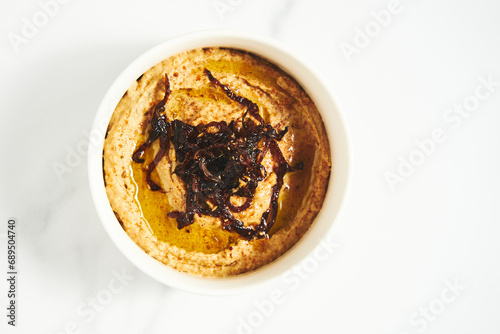 Foto Hummus with caramelized onions in white bowl on light background