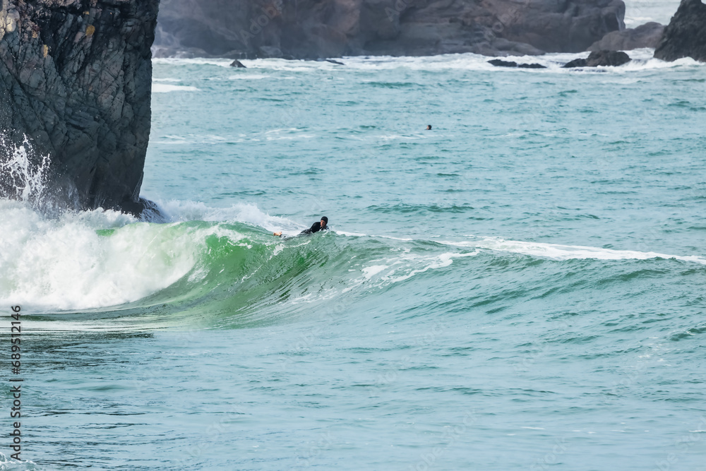 Fototapeta premium San Francisco, California, USA - October 23, 2021, A surfer rides a wave with cliffs in the background in San Francisco.