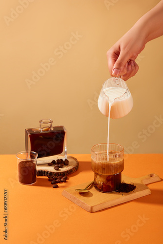 The hand is holding a glass of milk pouring into a cup of coffee, surrounded by coffee beans, coffee powder and black coffee. Coffee helps reduce the risk of Alzheimer's disease and dementia.