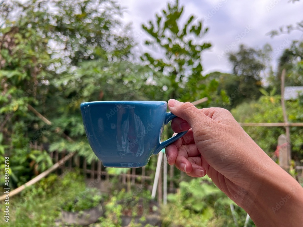 Hand holding a hot coffee ceramic cup in the morning nature background.
