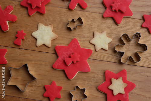 Christmas background with many star shaped shortcrust cookies with red sugar glaze and metallic cookie cutters on a wooden table