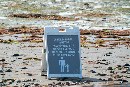 Child Supervision Warning Sign on a Pebbled Beach Shore