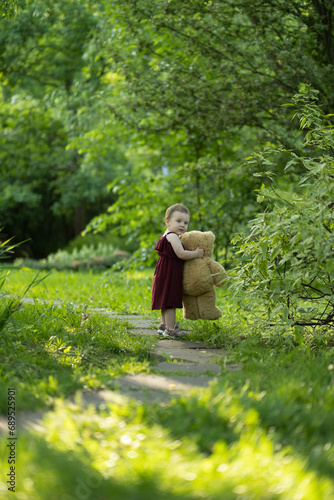 The image of a child's first independent strides into nature, teddy bear in arm, captures the essence of youthful discovery and the simple joys of a summer day. © yavdat