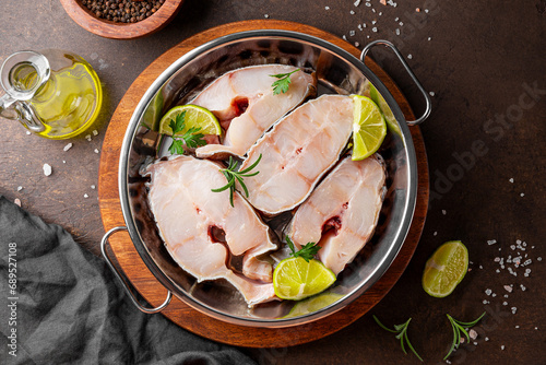 Raw catfish steaks with herbs, lime and spices in a baking dish on a dark background top view photo