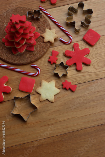 Christmas tree made of star shaped shortcrust cookies with red sugar glaze with cookie cutters candy canes and other cookies on wooden table. Christmas background