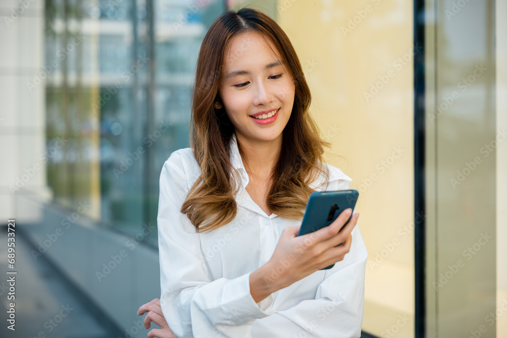 An Asian girl is enjoying the outdoors while using her smartphone. She is swiping and typing on the device. The woman is connected and engaged. An Asian girl is enjoying the outdoors while using her smartphone. She is swiping and typing on the device. The woman is connected and engaged.