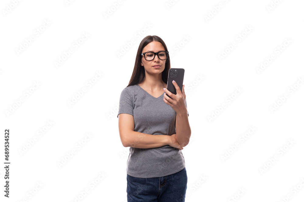 © Ivan Traimak - young cute brunette european woman dressed in a gray t-shirt uses a mobile phone on a white background