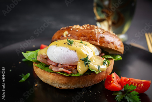 Breakfast. Sandwich with ham, poached egg, onion and arugula in a plate on a dark background
