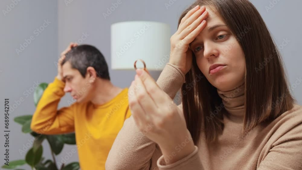 Attractive serious woman removing wedding ring from finger despaired husband sitting on background with negative sad feelings couple having problems in relationship thinking about divorce Attractive serious woman removing wedding ring from finger despaired husband sitting on background with negative sad feelings couple having problems in relationship thinking about divorce