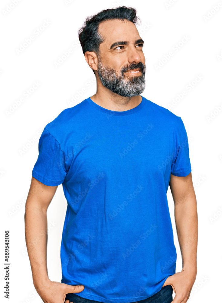 Middle aged man with beard wearing casual blue t shirt looking away to side with smile on face, natural expression. laughing confident. Middle aged man with beard wearing casual blue t shirt looking away to side with smile on face, natural expression. laughing confident.