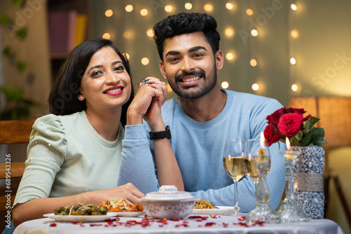Happy smiling couple holding hands by looking at camera during candle light dinner at home - concept of valentine s day  love and relationship.