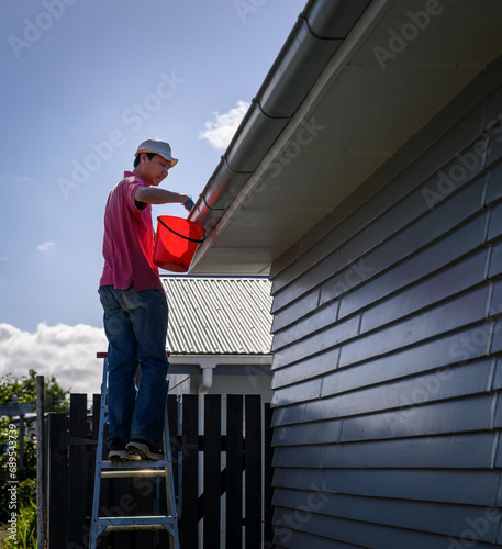 Obraz na płótnie Man standing on the ladder and cleaning the gutter. Home maintenance work. Vertical format. Auckland. w salonie
