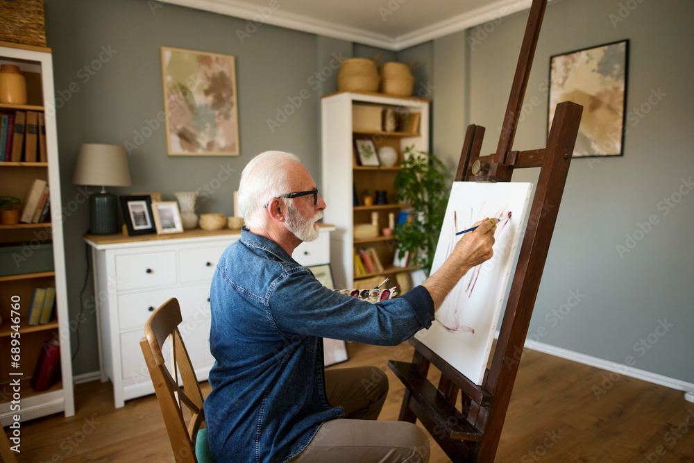 Elderly man painting on a canvas at home