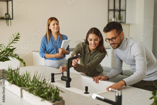 Female shop assistant helping young couple choose new kitchen faucet photo