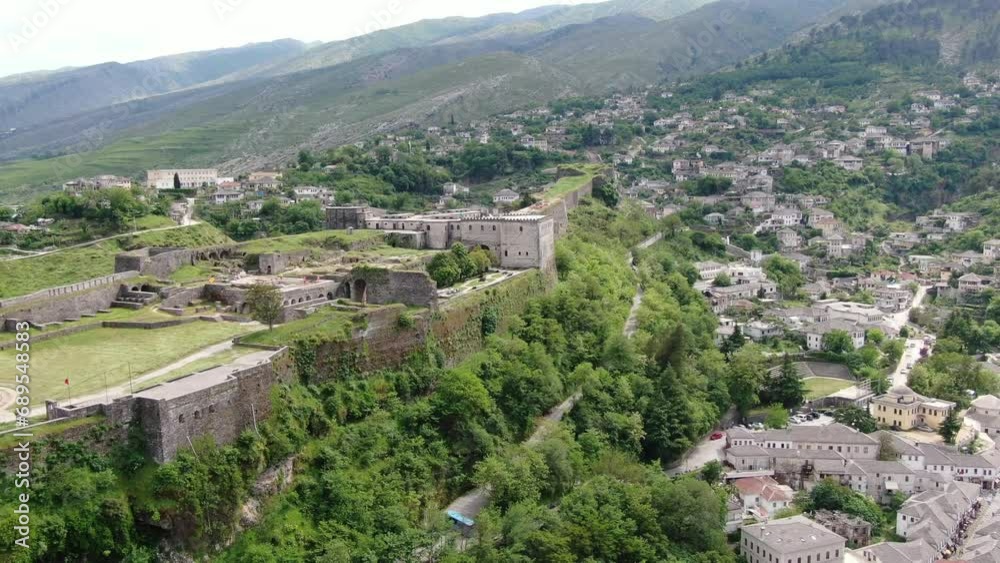 Drone view in Albania flying in Gjirokaster town over a medieval castle on high ground fort showing the brick brown roof houses Drone view in Albania flying in Gjirokaster town over a medieval castle on high ground fort showing the brick brown roof houses