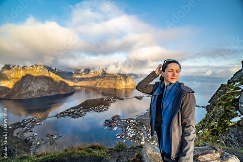 A young woman is scratching the back of her head with a contemplative expression from the height of Reinebringen on fisherman reine village on lofoten islands in norway photo