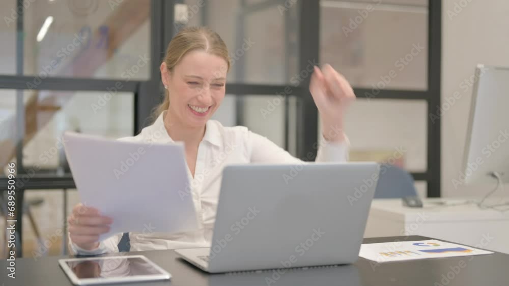 Mature Business Woman Celebrating while Using Laptop and Documents