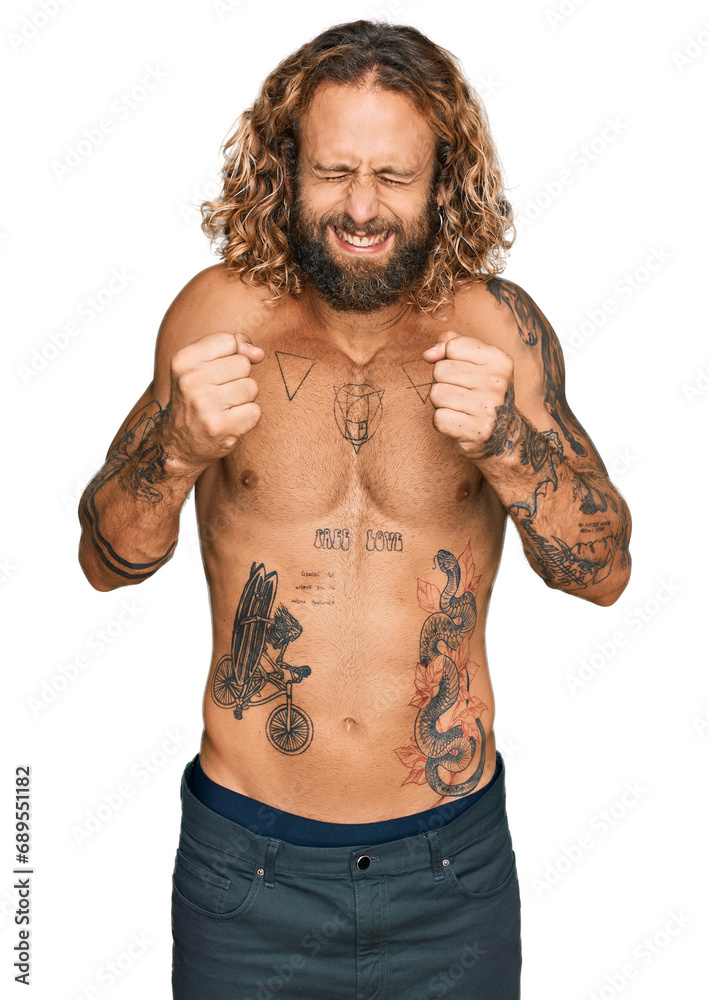 Handsome man with beard and long hair standing shirtless showing tattoos excited for success with arms raised and eyes closed celebrating victory smiling. winner concept. Handsome man with beard and long hair standing shirtless showing tattoos excited for success with arms raised and eyes closed celebrating victory smiling. winner concept.