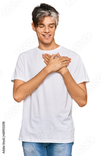 Young hispanic man wearing casual white tshirt smiling with hands on chest with closed eyes and grateful gesture on face. health concept.