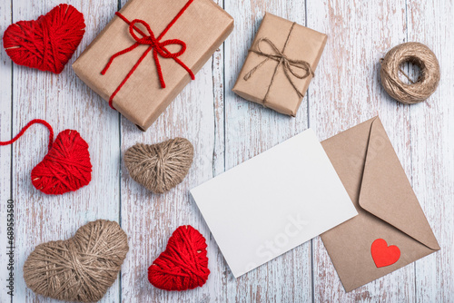 Craft envelope, blank form, heart shapes made of red threads and twine and two craft gift boxes and on a wooden background. DIY gifts for Valentine's Day.