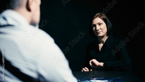 Canvas Print A detective is showing photos of the crime scene to a woman suspect, and she den