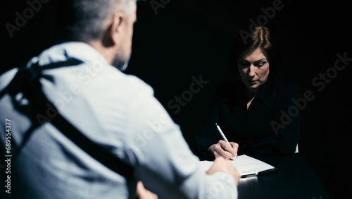 A sad woman is confessing a crime to a police detective and signing a confession on paper photo