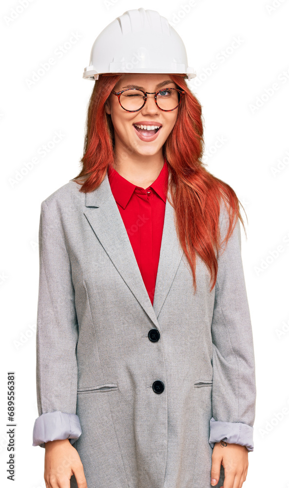 Young redhead woman wearing architect hardhat winking looking at the camera with sexy expression, cheerful and happy face.