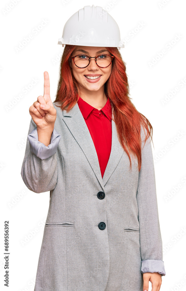 Young redhead woman wearing architect hardhat showing and pointing up with finger number one while smiling confident and happy. Young redhead woman wearing architect hardhat showing and pointing up with finger number one while smiling confident and happy.