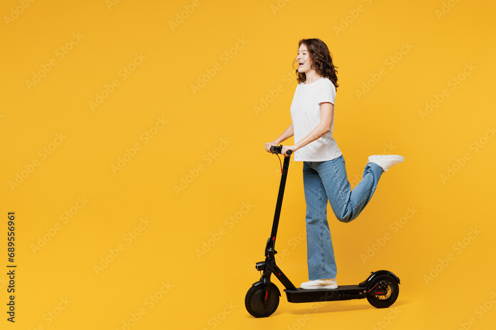 Side profile view young European woman she wear white blank t-shirt casual clothes driving electric scooter look camera isolated on plain yellow orange background studio portrait. Lifestyle concept. - obrazy, fototapety, plakaty 