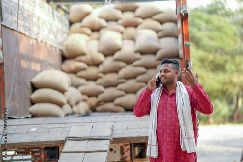 Sacks of grain are kept in the food market and the farmer is happily talking on the phone.