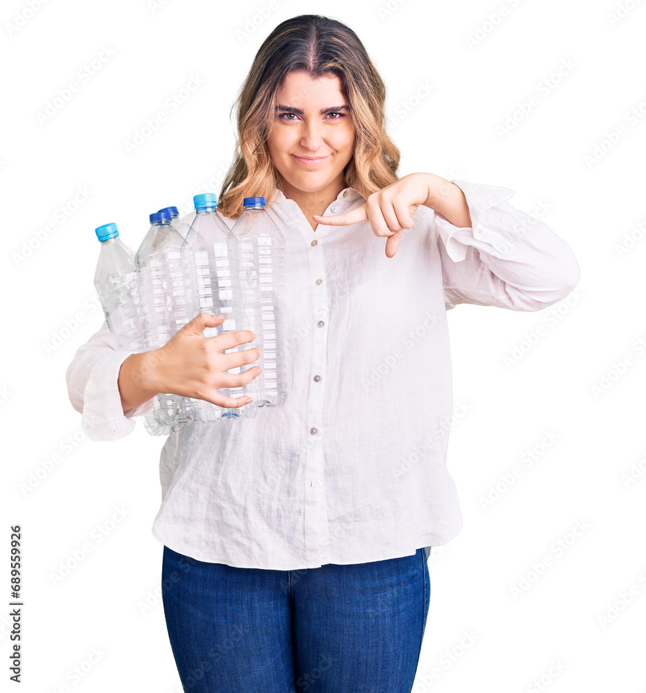 Young caucasian woman holding recycling plastic bottles smiling happy pointing with hand and finger Young caucasian woman holding recycling plastic bottles smiling happy pointing with hand and finger