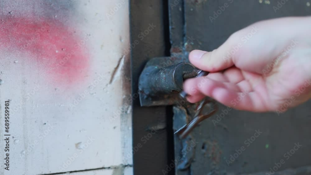 Unscrewing the old blockage lock on the iron door of the black garage. Protection against intrusion and theft, close-up. Slow motion Unscrewing the old blockage lock on the iron door of the black garage. Protection against intrusion and theft, close-up. Slow motion
