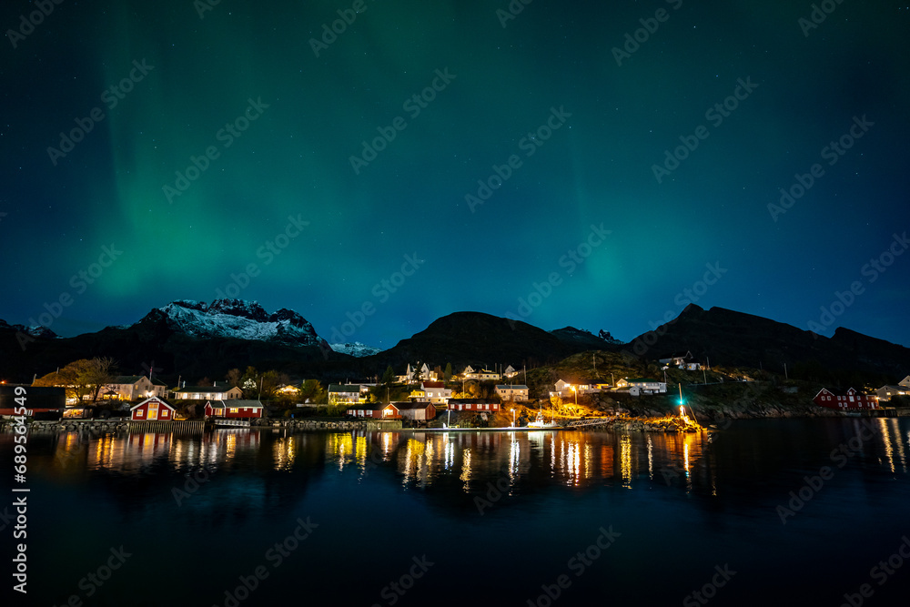 bright aurora borealis over a small coastal Sørvågen village on lofoten islands in norway with mountains on background