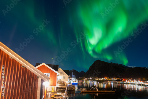 bright aurora borealis over a small coastal Sørvågen village on lofoten islands in norway with mountains on background © Sid Smith